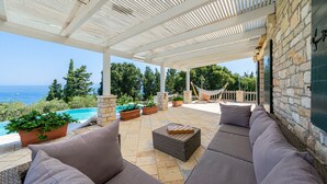 A covered outdoor seating area with a view of the sea, stone walls, and potted plants.