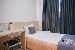 Ett hotellrum med en säng, ett skrivbord, en stol, ett fönster med gardiner och en liten växt på skrivbordet.