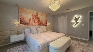 Une chambre à coucher avec un grand lit, un banc, une table de chevet, un lustre, une fresque murale et une porte.