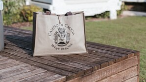 Een houten terras met een witte zithoek en een tas met de tekst 'CASINO DI CACC' WINE RESORT.