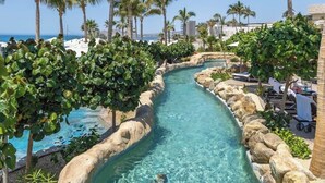 A clear water channel with rocks on the sides, surrounded by lush greenery and palm trees, leading to a beach area with sun loungers. - Charming 1-bedroom villa beach front, Thanksgiving week in San José del Cabo (San José del Cabo)