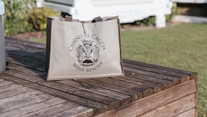 Una terraza de madera con un área de estar exterior blanca y un bolso con la etiqueta 'CASINO DI CACC' WINE RESORT.