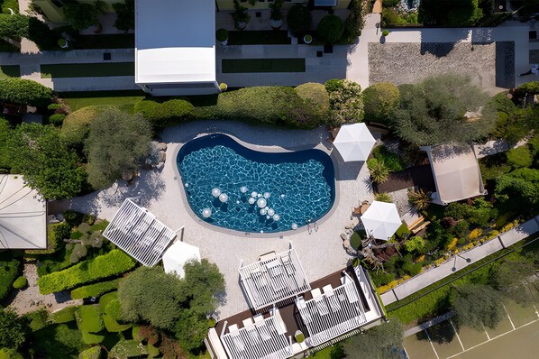 An aerial view of a hotel with a central swimming pool, surrounded by greenery and white structures.