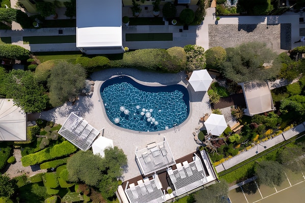 An aerial view of a hotel with a central swimming pool, surrounded by greenery and white structures.
