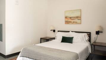 Un dormitorio con una cama, dos mesitas de noche, una lámpara de pared, un cuadro y una alfombra estampada.