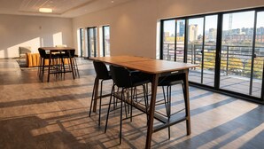 A spacious room with a large table and chairs, large windows with a city view, and a high ceiling with recessed lighting. - Deer District Studio Apt - One Block from Fiserv and Baird (Milwaukee)