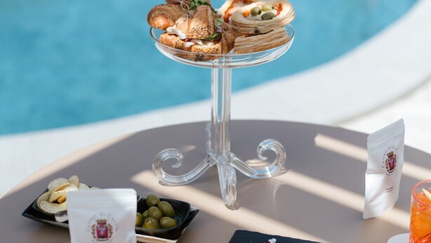 Ein Tisch am Pool mit einer Dessertauslage, einem Getränk und einer Olivenplatte.