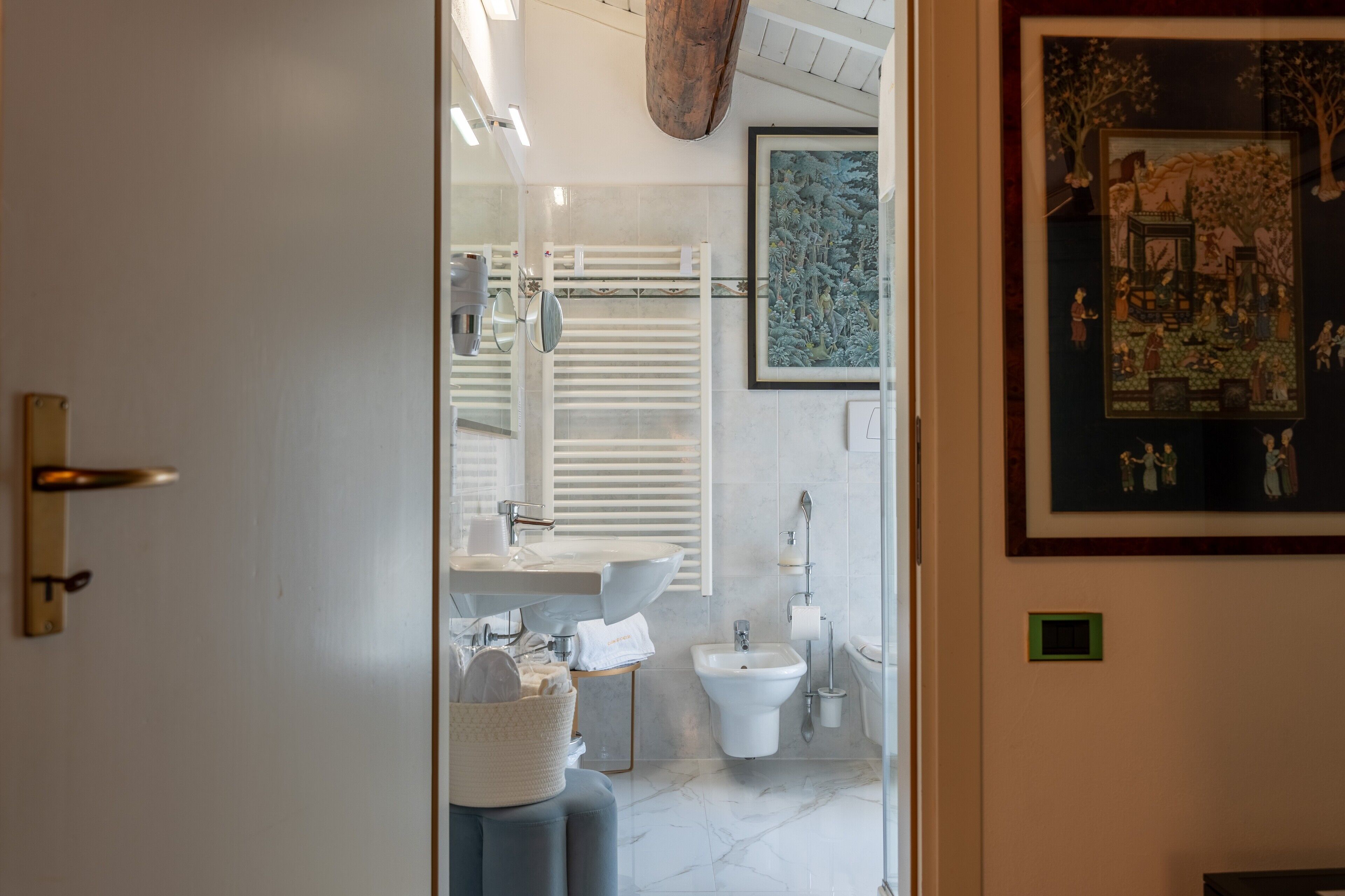 Une salle de bain moderne avec un lavabo, des toilettes et un bidet blancs, un miroir et une œuvre d’art encadrée accrochée au mur.