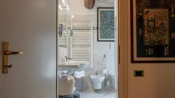 Une salle de bain moderne avec un lavabo, des toilettes et un bidet blancs, un miroir et une œuvre d’art encadrée accrochée au mur.