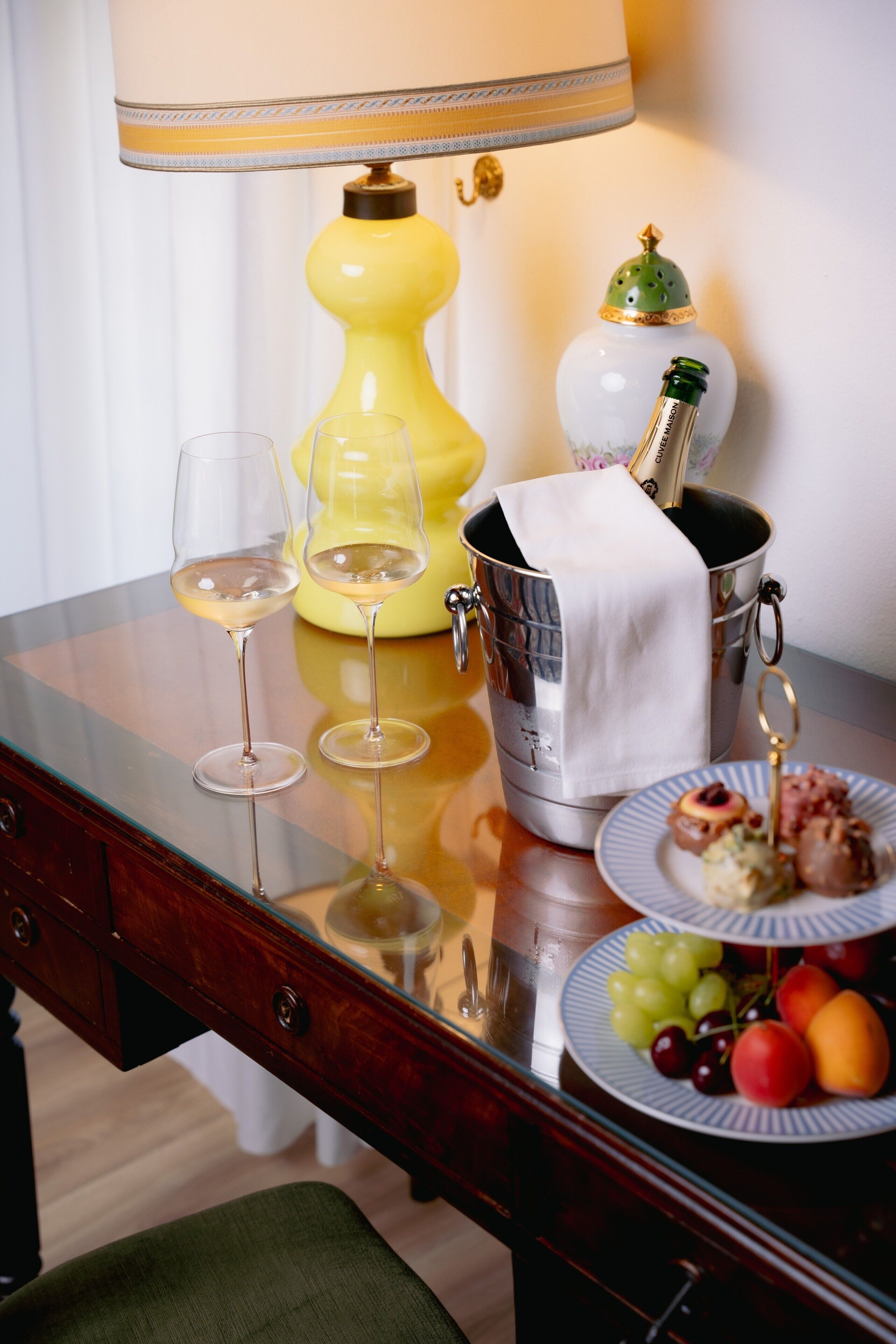Ein Tisch mit zwei Weingläsern, einer Champagnerflasche, einer Obstplatte und einer gelben Lampe.