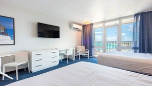 Ett hotellrum med två sängar, ett skrivbord, en stol, en TV och ett stort fönster med utsikt över havet.