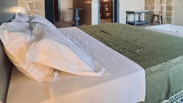 A bedroom with a stone arch ceiling, a bed with a green blanket, and a small table with a chair. - King Room with Jacuzzi - Charming in Felline - Borgo Don Ciccio (Felline)