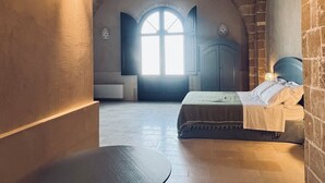 A room with a vaulted ceiling, a bed, a round table, and a large window. - King Room with Jacuzzi - Charming in Felline - Borgo Don Ciccio (Felline)
