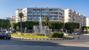 Un edificio de varios pisos con una fuente en el centro, rodeado de vegetación y un paseo peatonal.