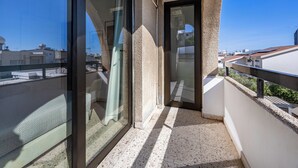A balcony with a glass door, a view of the cityscape, and a tiled floor.