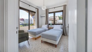 A modern bedroom with two single beds, a small desk, and a chair.