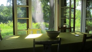 Ein Esstisch mit Schüssel und Buch, vor großen Fenstern mit Blick auf Grünflächen.