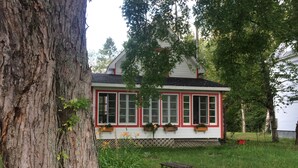 Ein Haus mit weißer Fassade und roten Akzenten, umgeben von einem grünen Rasen und Bäumen.