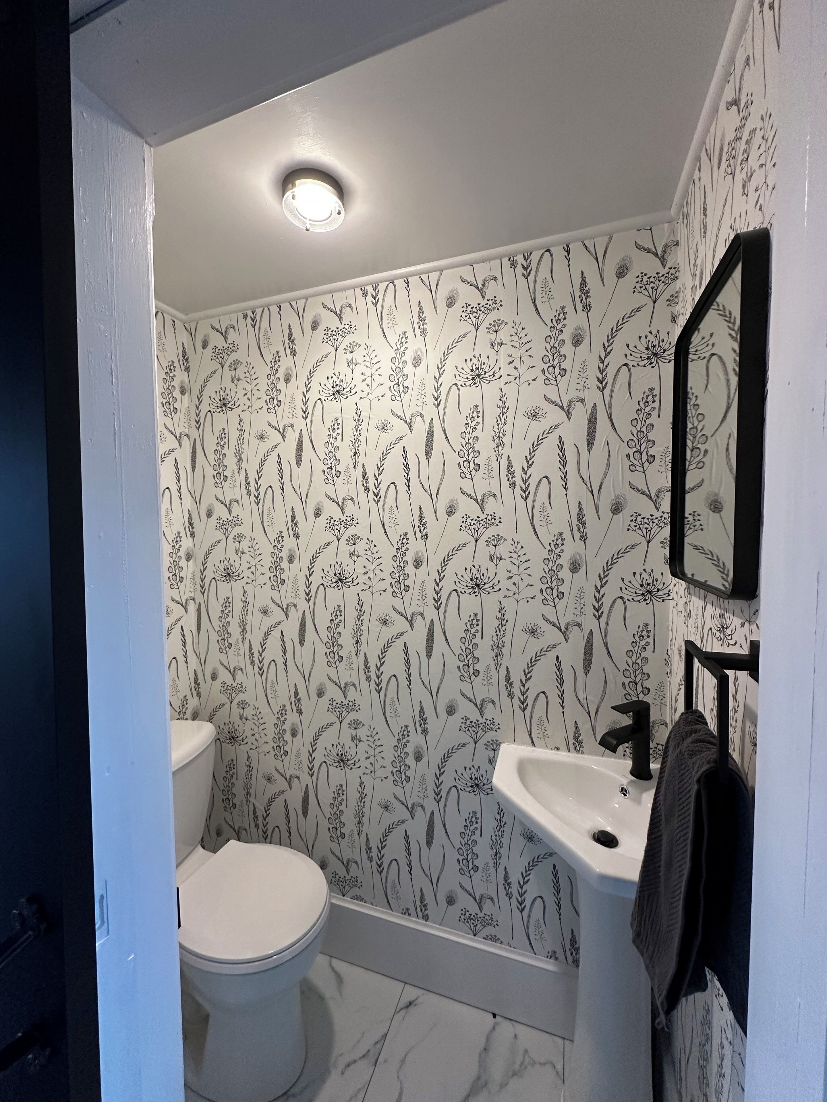 Un baño con inodoro, lavabo y espejo. Las paredes tienen un estampado de papel tapiz floral.