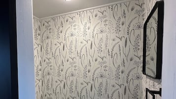 Un baño con inodoro, lavabo y espejo. Las paredes tienen un estampado de papel tapiz floral.