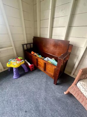 Una habitación lateral con un banco de madera, una mesita con juguetes y una silla de mimbre.