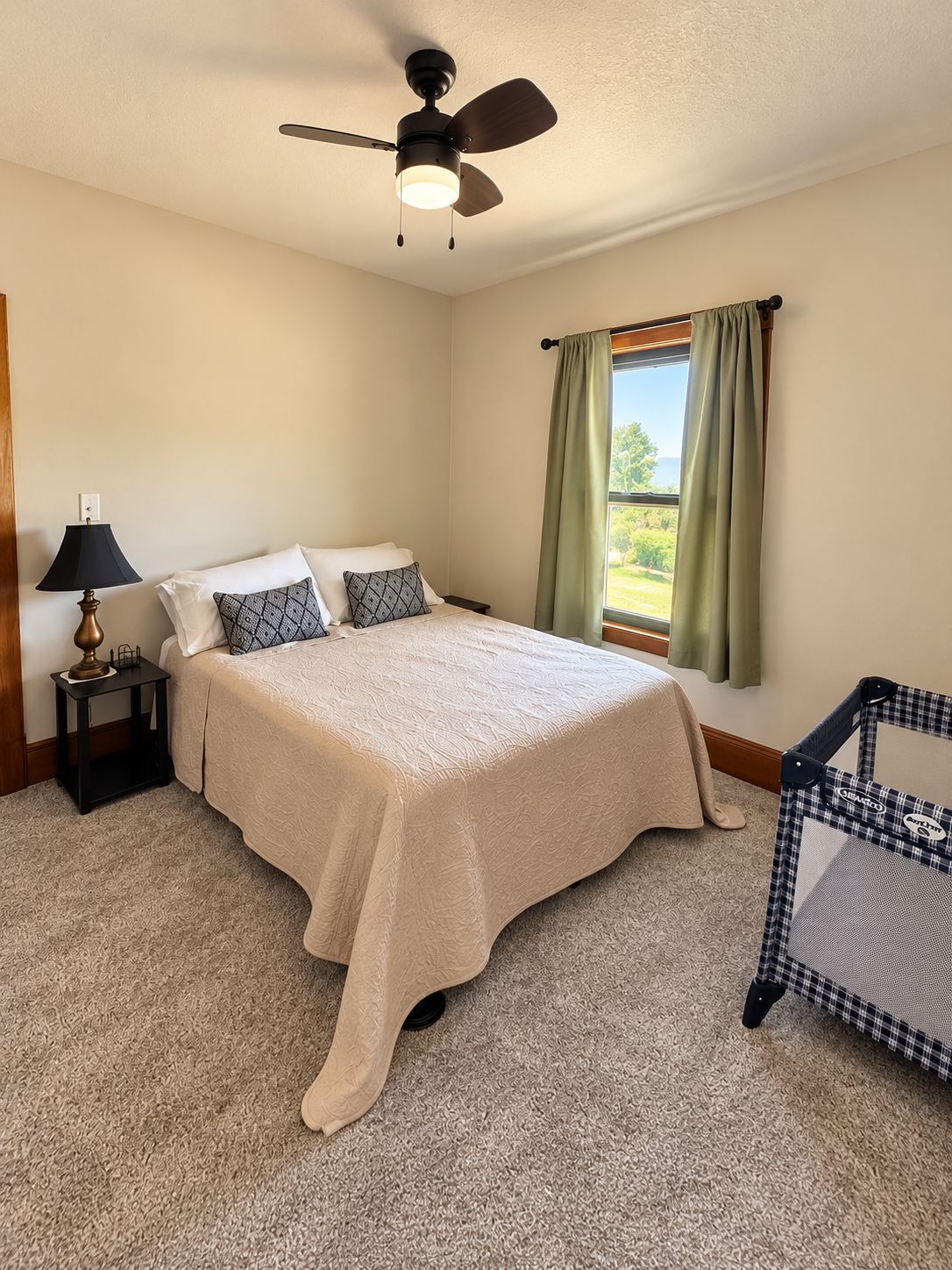 A bedroom with a bed, a nightstand, a lamp, a window with curtains, and a ceiling fan.