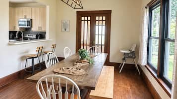 A dining area with a wooden table, white chairs, and a kitchen in the background.