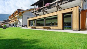Un bâtiment moderne doté de grandes fenêtres, de balcons en bois ornés de jardinières et d’une pelouse bien entretenue.