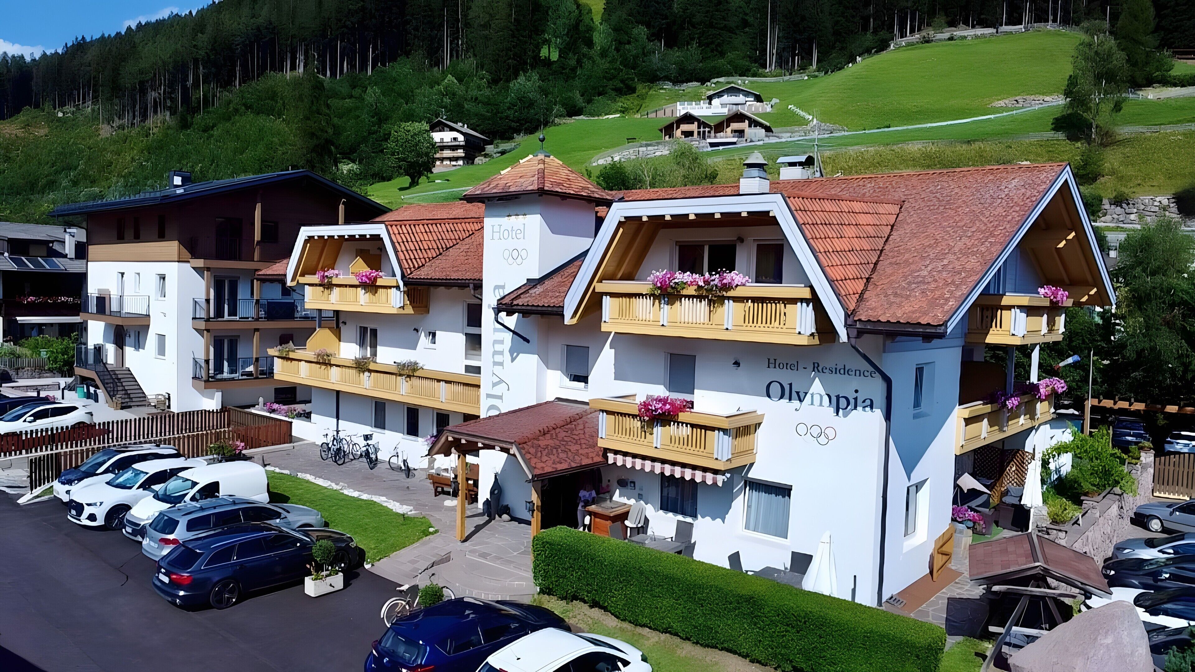 A hotel with a traditional Alpine architectural style, featuring balconies with flower boxes and a sign indicating it is a hotel.