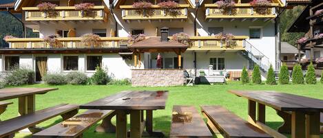 A hotel with multiple balconies adorned with flowers, a stone facade, and outdoor wooden picnic tables.