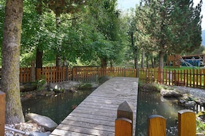 Un pont en bois enjambant une étendue d’eau calme, entouré d’arbres et d’une clôture en bois.