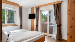 Une chambre avec un lit, une télévision, des poutres en bois, une fenêtre et une porte-fenêtre coulissante donnant sur un espace extérieur.
