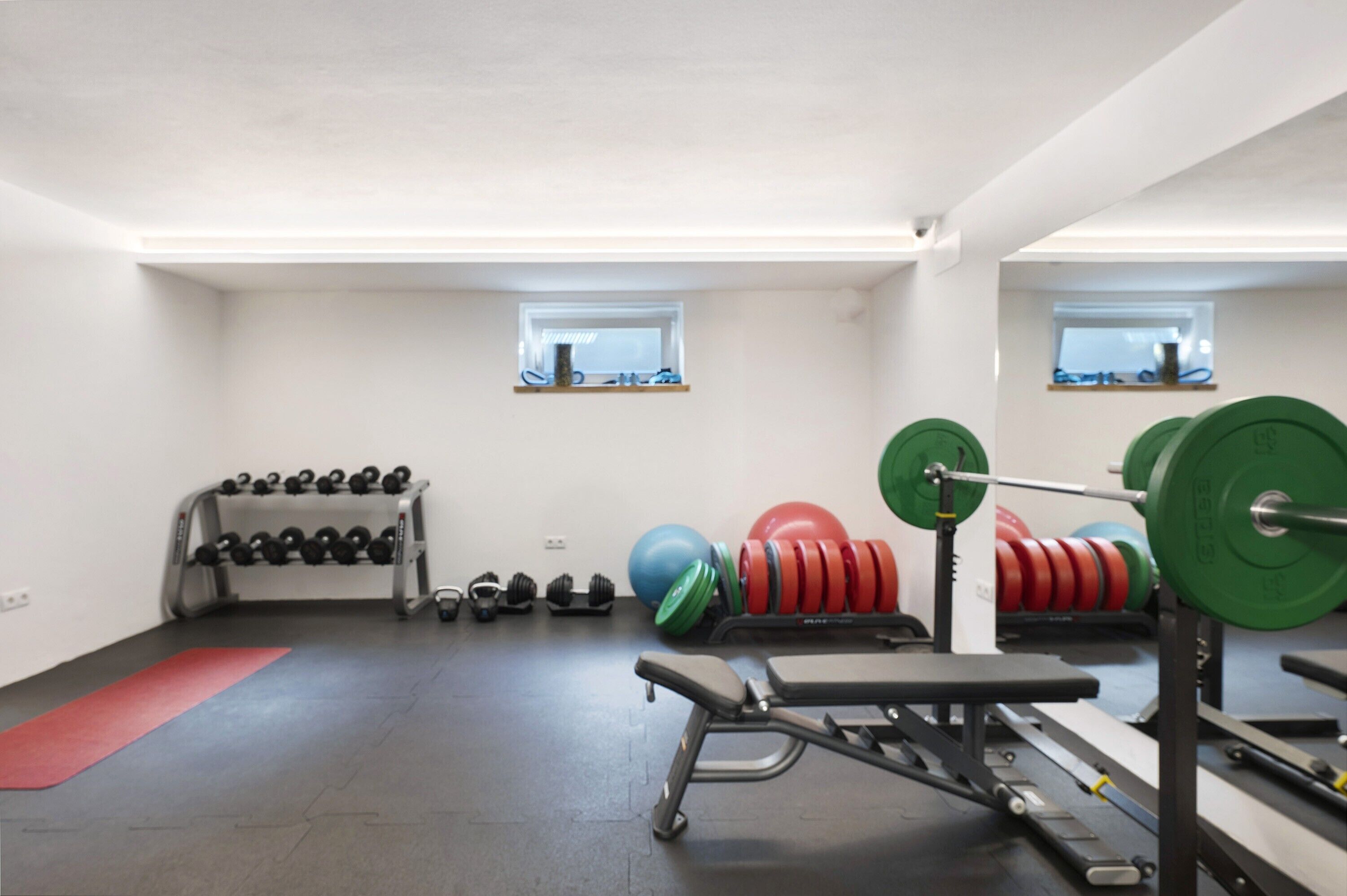 Un gimnasio con equipo de levantamiento de pesas, una banca y mancuernas.