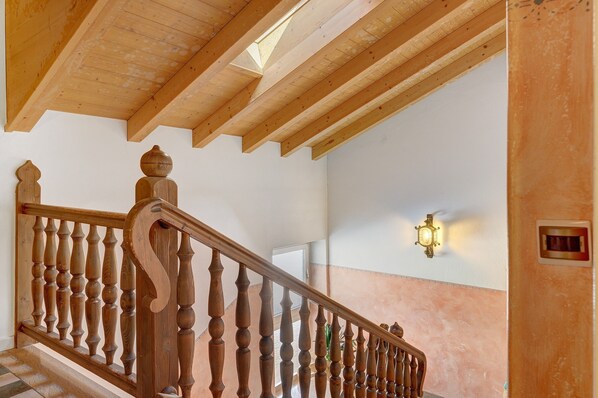 A wooden staircase with balusters and a handrail, a light fixture on the wall, and a window in the background.
