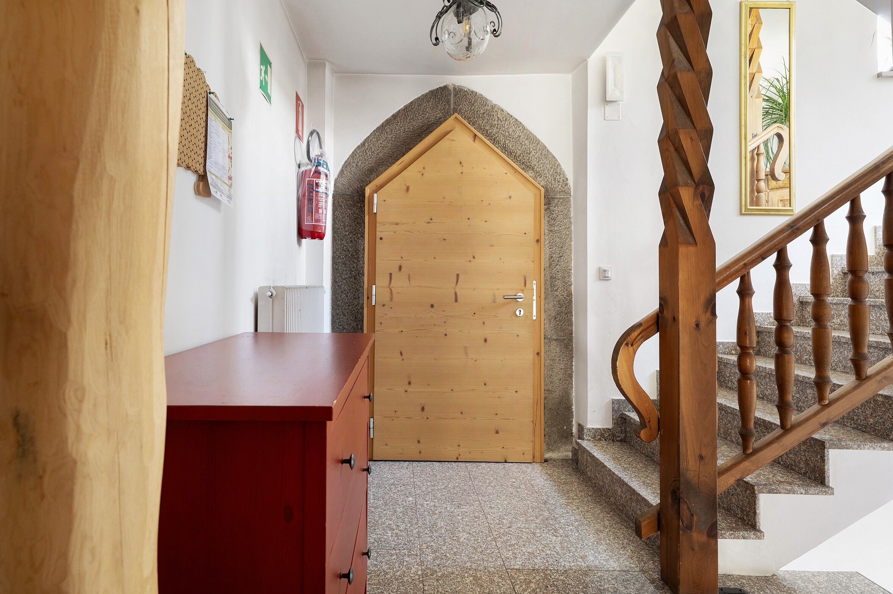 A wooden door with a stone archway, a red cabinet, and a staircase with wooden balusters.