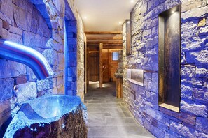 A stone-walled hallway with a glass bathtub and a metal pipe.