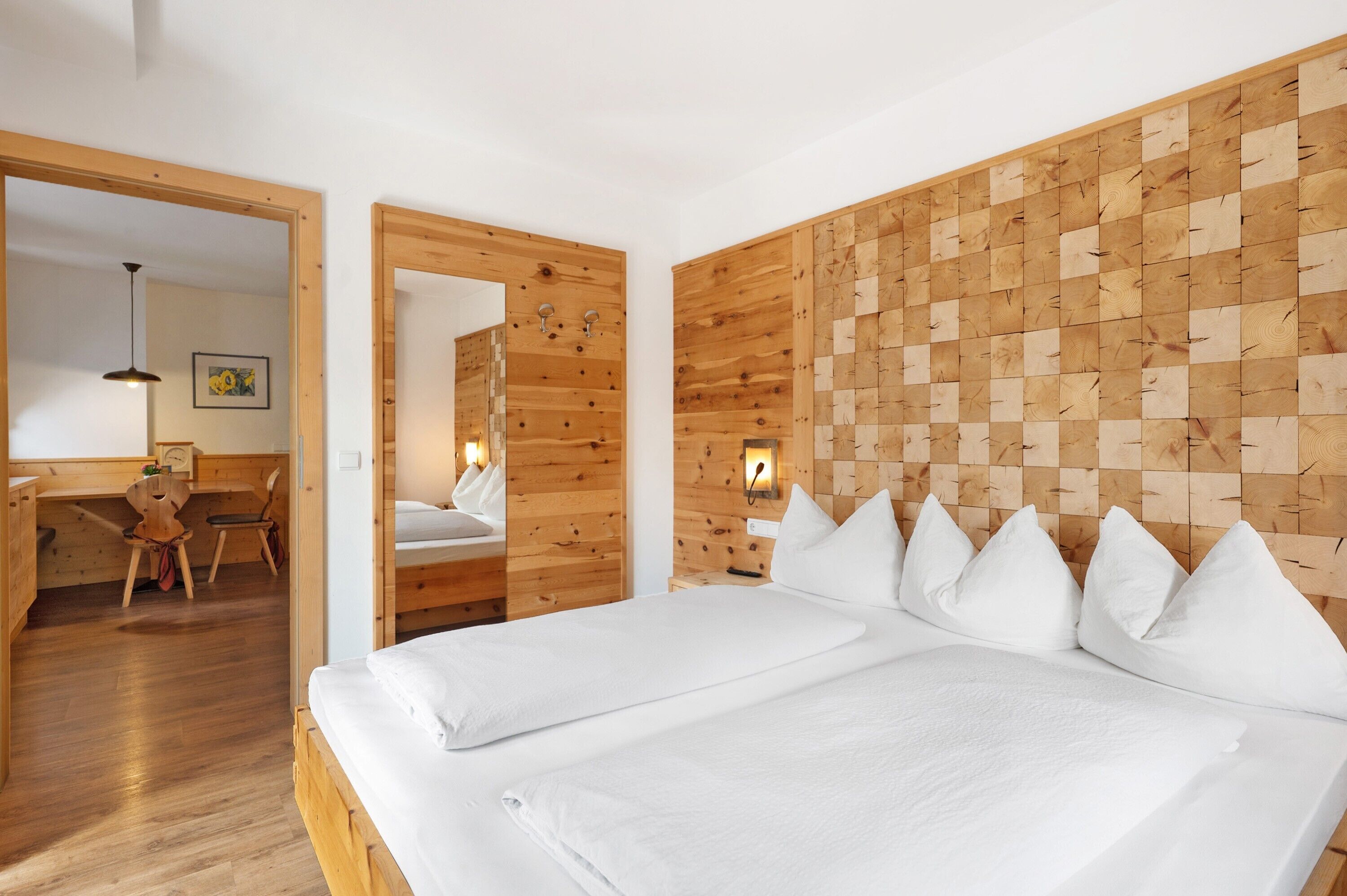 A room with a wooden headboard, a bed with white bedding, a desk with a chair, and a mirror.