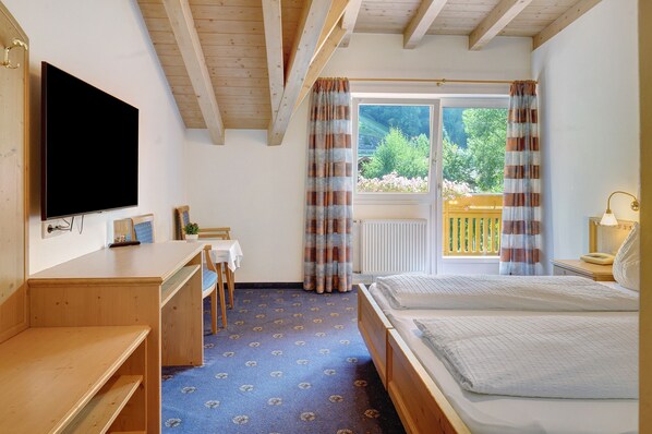 Een slaapkamer met een bed, een bureau, een televisie en een raam met gordijnen.