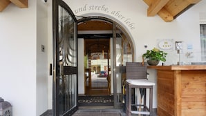 A hotel entrance with a glass door, a wooden bench, a potted plant, and a sign reading 'Hotel Olympia.'