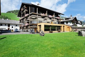 A multi-story building with balconies, a large glass window, and a stone wall. - Room 'Olympia Zimmer 204' with Mountain View, Shared Garden and Wi-Fi (Sarnthein)