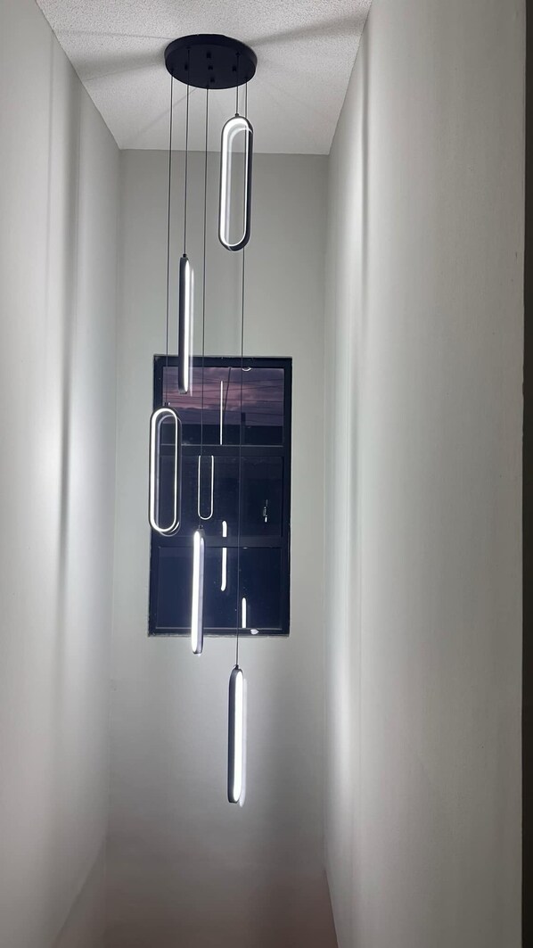 A modern interior with a minimalist design, featuring a ceiling-mounted light fixture with multiple hanging elements.