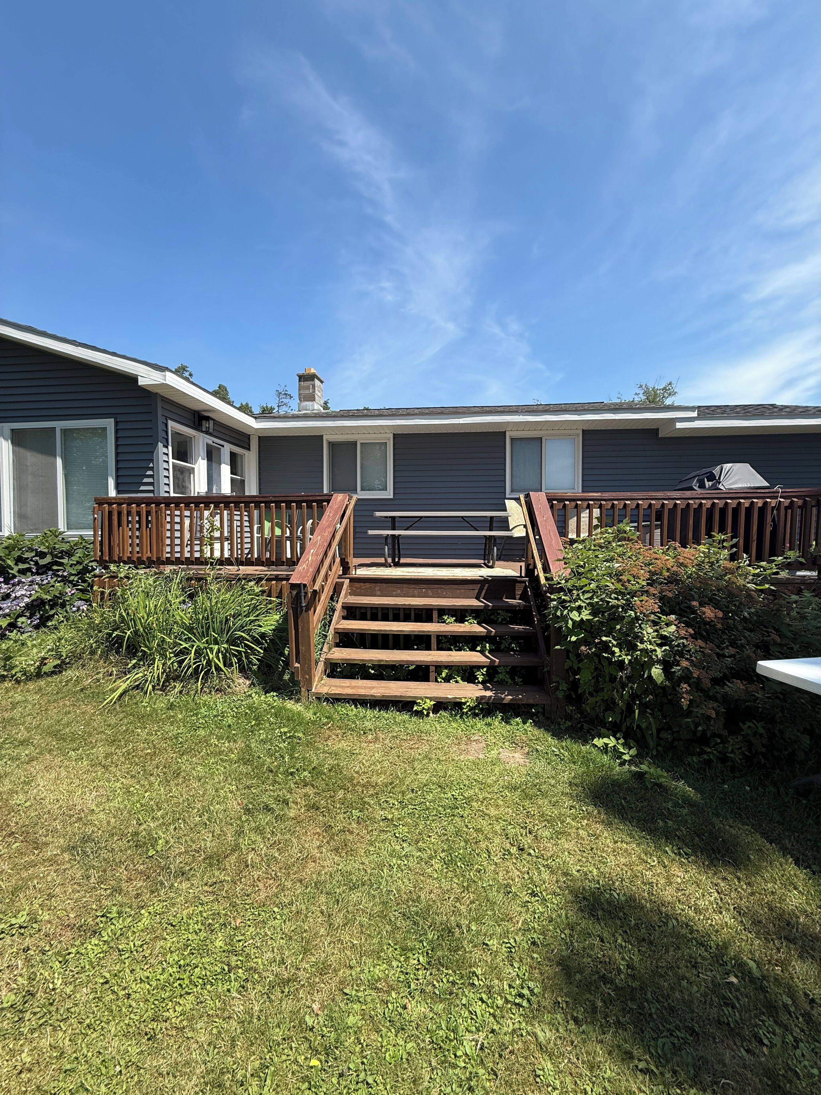 A residential property with a wooden deck, a set of stairs leading to a covered patio area, and a well-maintained lawn.