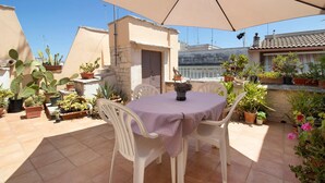 An outdoor patio with a table and chairs under a large umbrella, surrounded by potted plants and a stone wall. - Attica B&B – 'Red' Room with Shared Terrace, Wi-Fi, and Air Conditioning (Terlizzi)