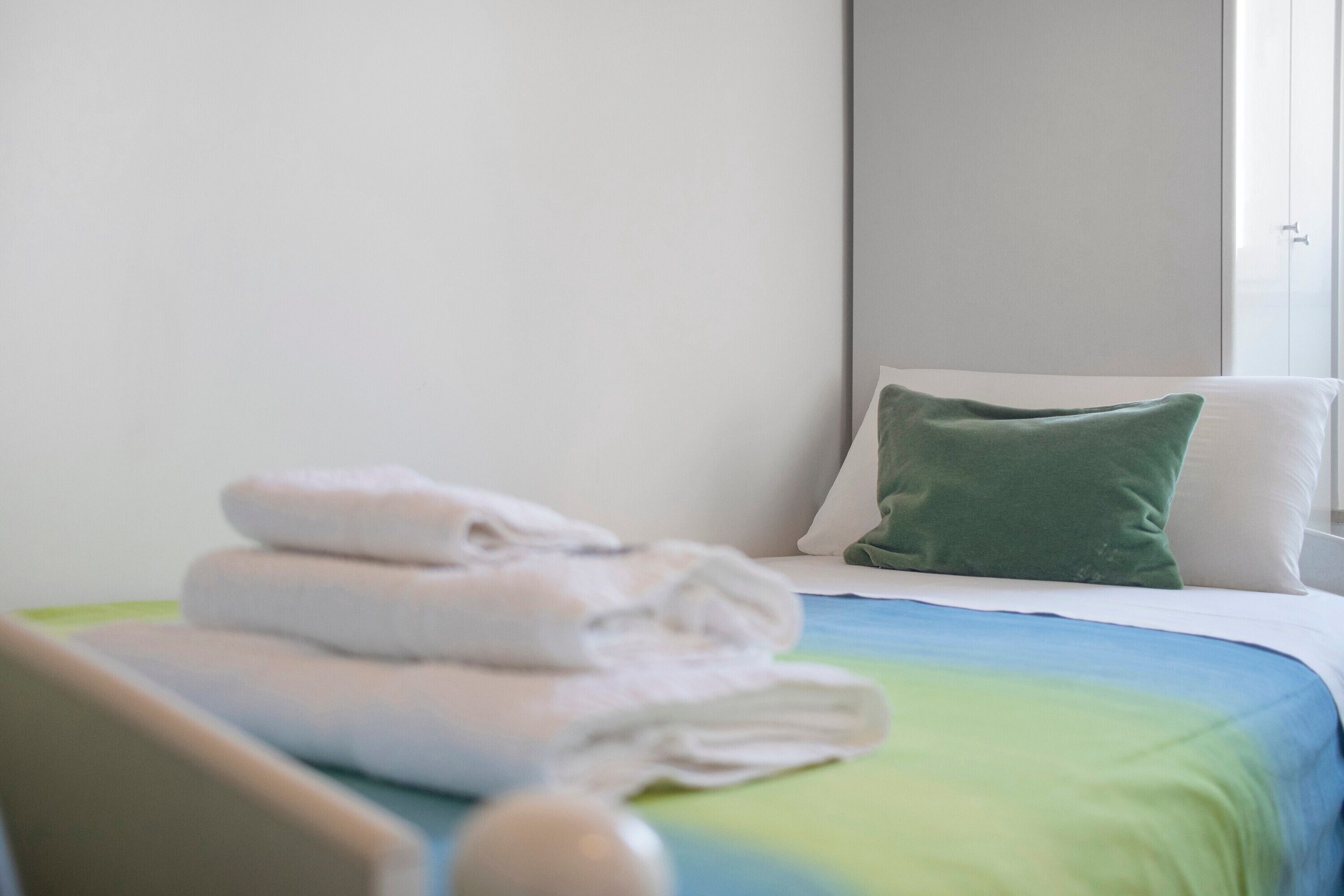 A hotel room with a bed, pillows, and folded towels.