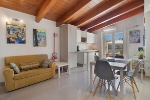 A modern living room with a sofa, a dining table, and chairs, a kitchen area, and artwork on the walls. - Attica BeB – 'Gialla' Room with Shared Terrace, Wi-Fi and Air Conditioning (Terlizzi)