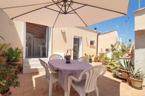 An outdoor patio with a table and chairs, surrounded by potted plants and a large umbrella. - Attica BeB – 'Gialla' Room with Shared Terrace, Wi-Fi and Air Conditioning (Terlizzi)