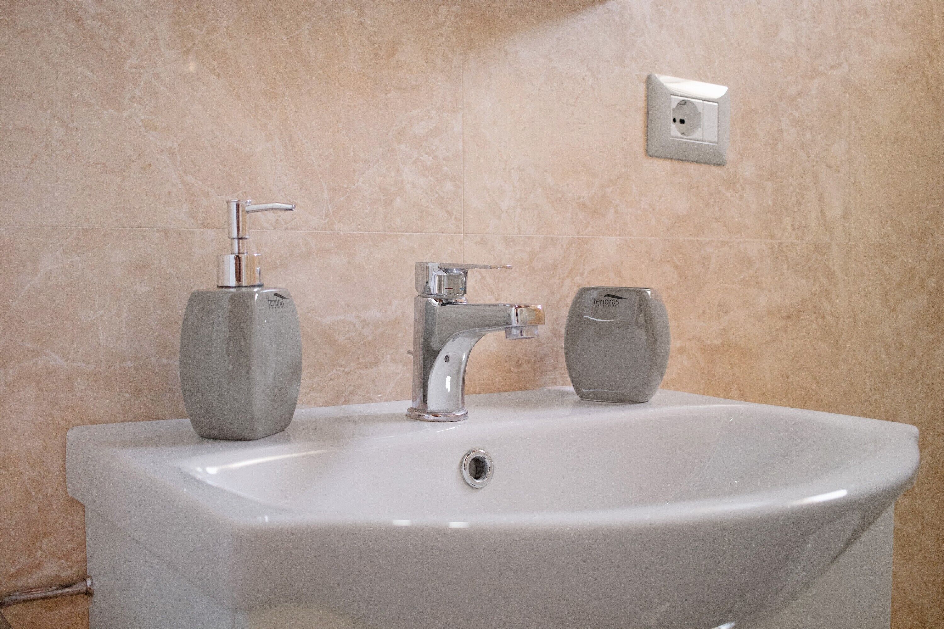 Ein Badezimmer mit einem weißen Waschbecken, einem chromfarbenen Wasserhahn und zwei Seifenspendern.