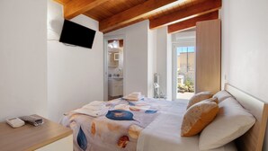Een slaapkamer met een bed, een aan de muur bevestigde televisie, een nachtkastje met een telefoon en oplader, en uitzicht op buiten.