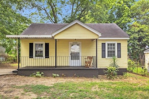 A yellow single-story house with a front porch, a number '203' on the door, and a small garden area. - Spacious Stay w 2 King Beds Minutes to Downtown (Greenville)