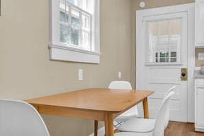 A room with a wooden table and white chairs, a window with blinds, and a door with a handle.